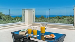 Un balcón con una mesa dispuesta para el desayuno, incluyendo dos vasos de zumo de naranja, una jarra y bollería.