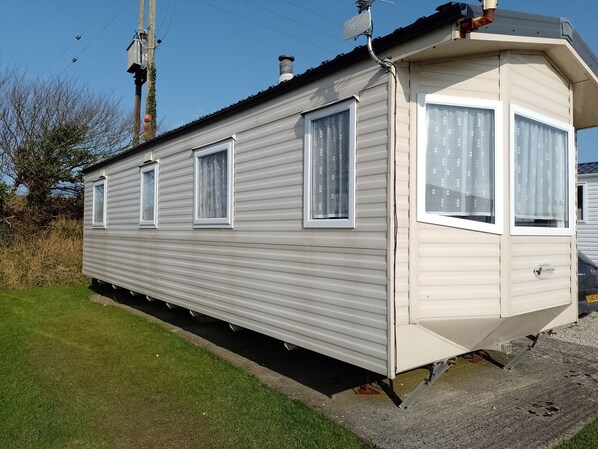 A single-story mobile home with a flat roof, multiple windows, and a visible chimney.