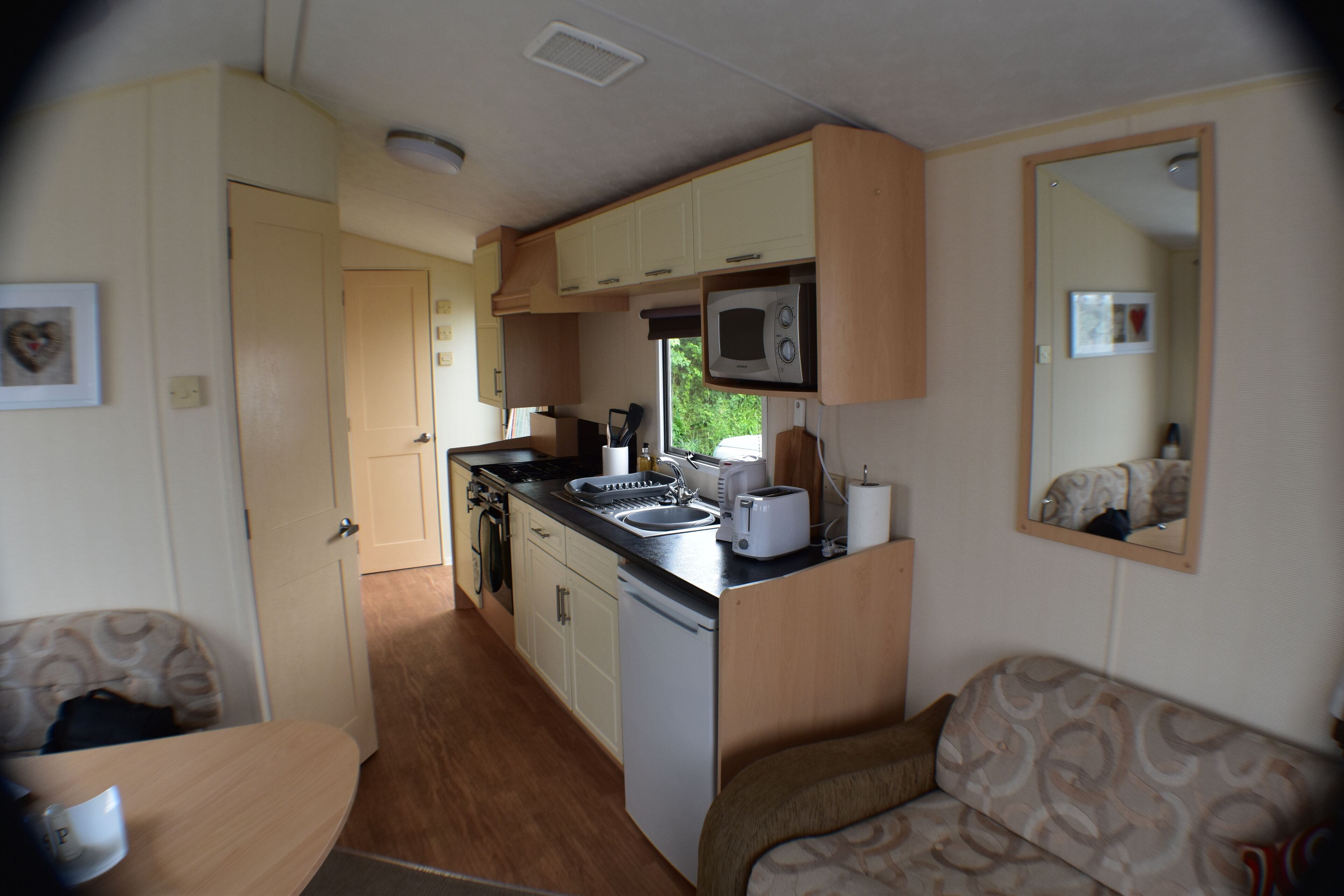 A compact RV kitchen with a microwave, sink, and small refrigerator. There is a dining area with a table and chairs.