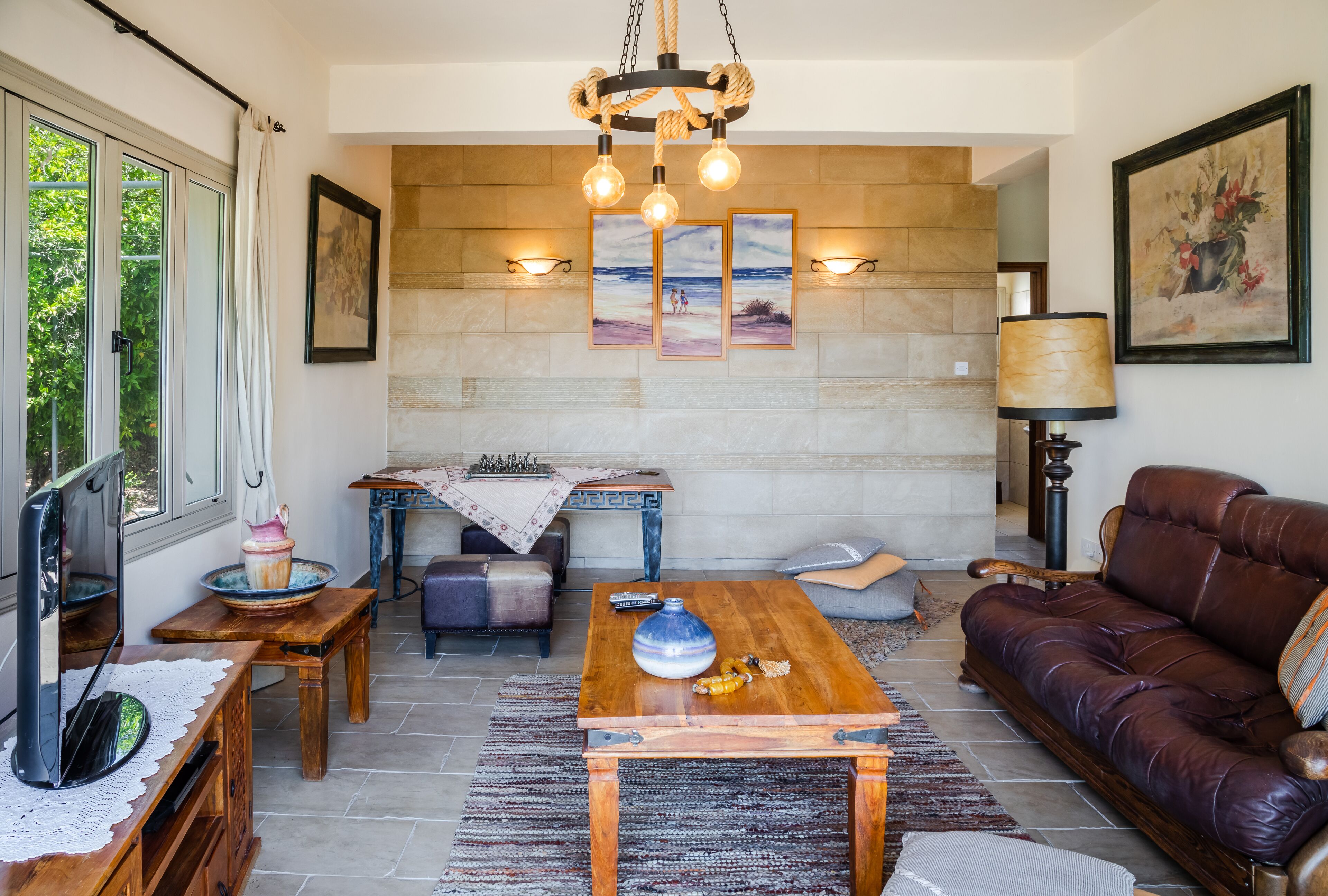 Una sala de estar con pared de piedra, un sofá de cuero marrón, una mesa de centro de madera y una araña.