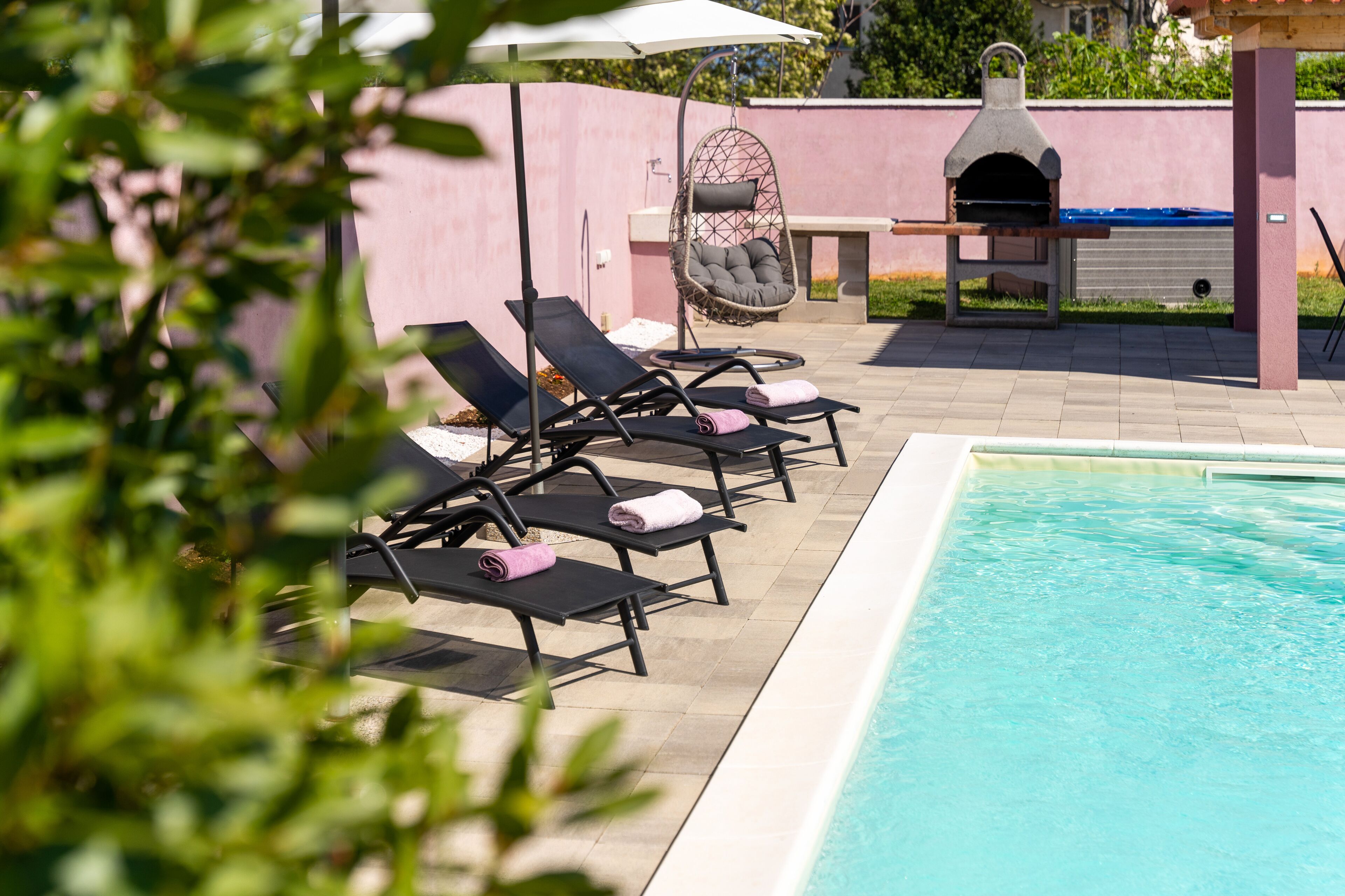 Un espace aménagé au bord de la piscine, avec des chaises longues, un fauteuil suspendu et un four à pizza.