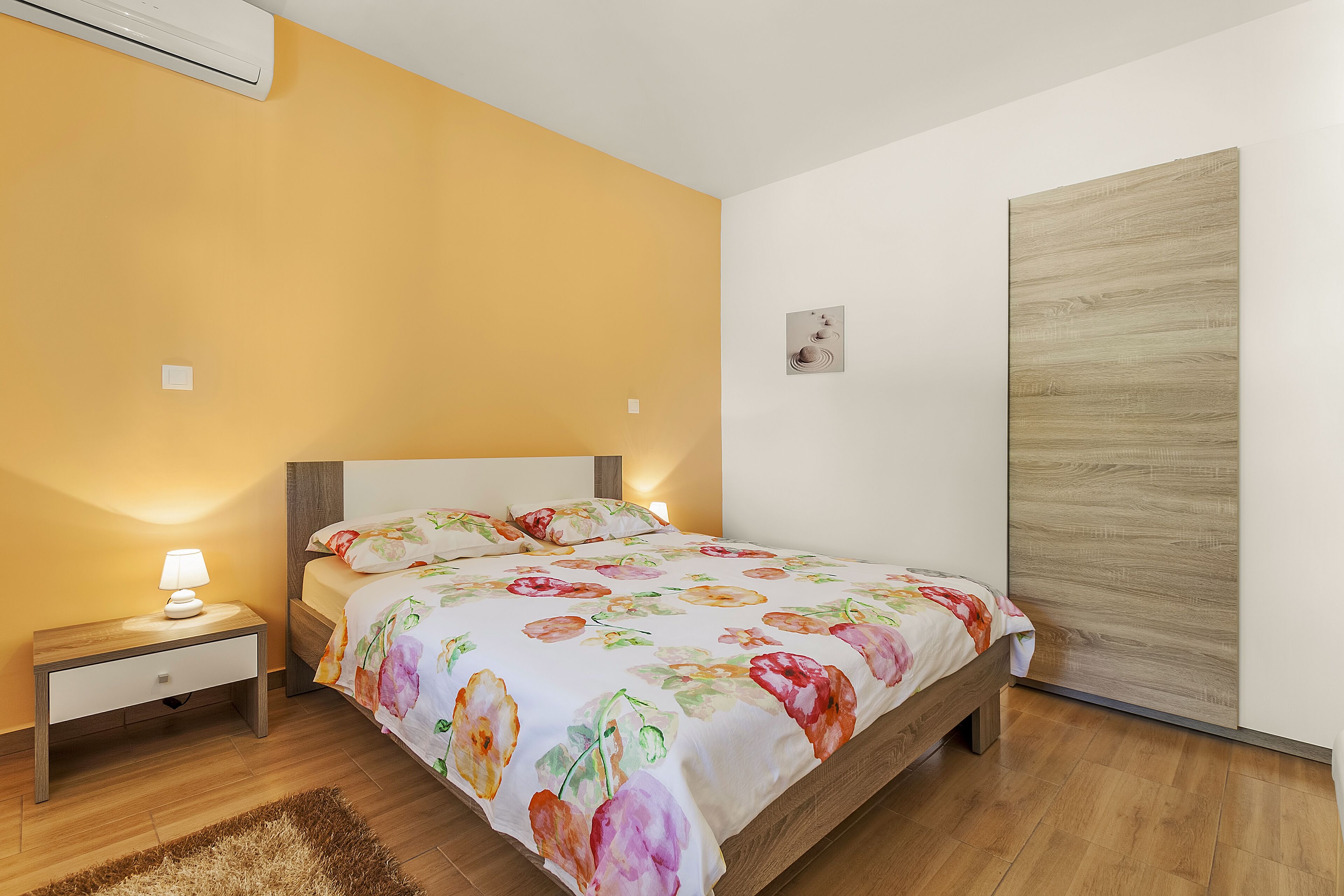 A bedroom with a bed, nightstand, lamp, and a wooden wardrobe.