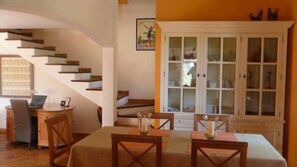 A dining area with a table set for two, a staircase, and a cabinet with glass doors.