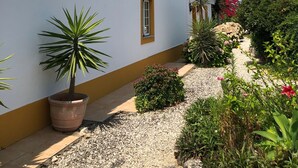 Un bâtiment blanc avec un toit recouvert de tuiles et un petit jardin agrémenté de diverses plantes et fleurs.