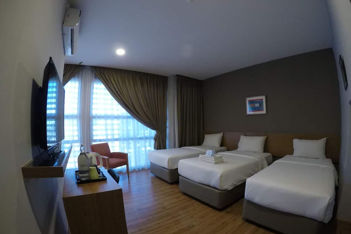 Quarto de hotel com duas camas de solteiro, uma escrivaninha com computador e cadeira, televisão e uma janela grande com cortinas.