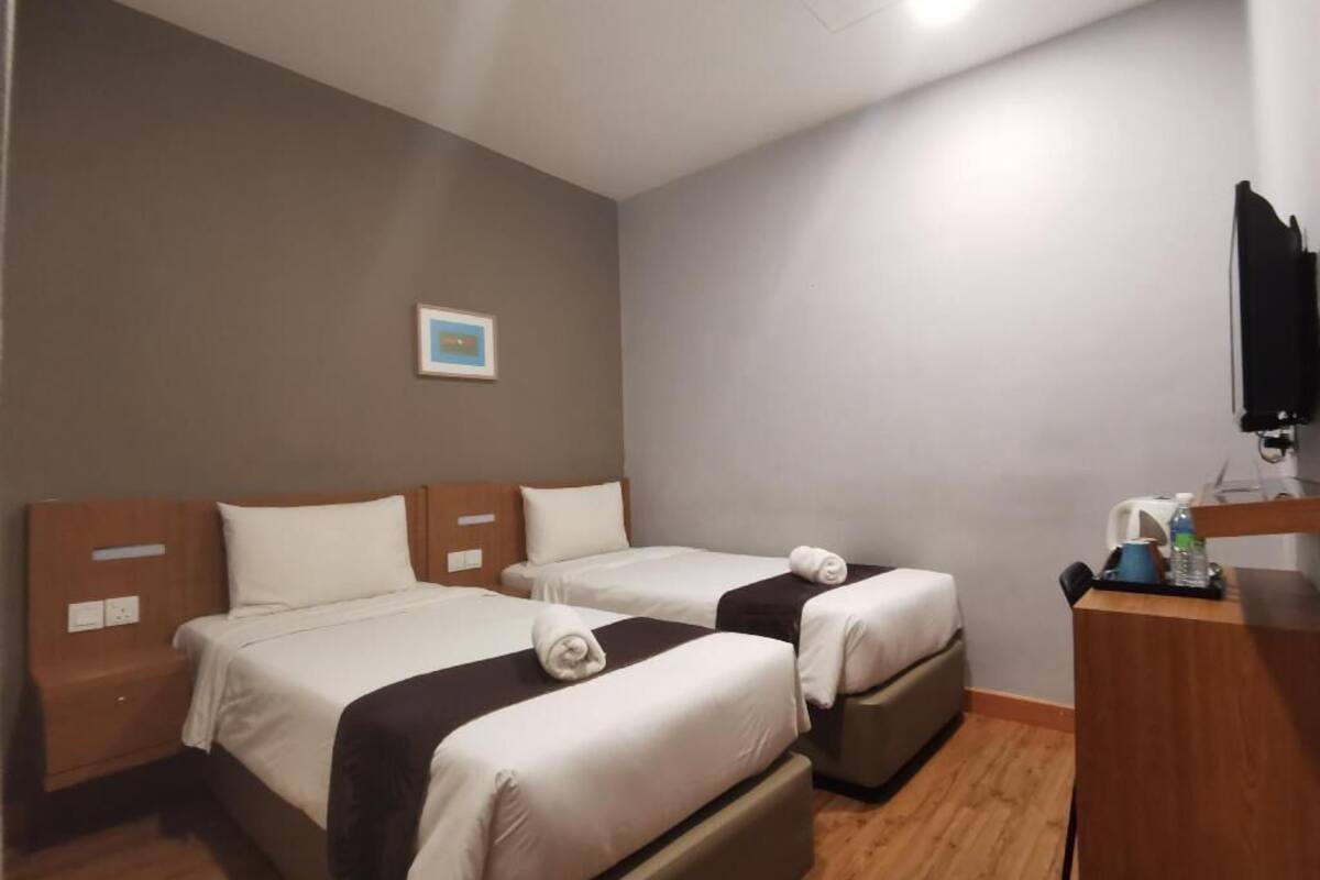 Quarto de hotel com duas camas, uma mesa, uma cadeira e uma televisão.