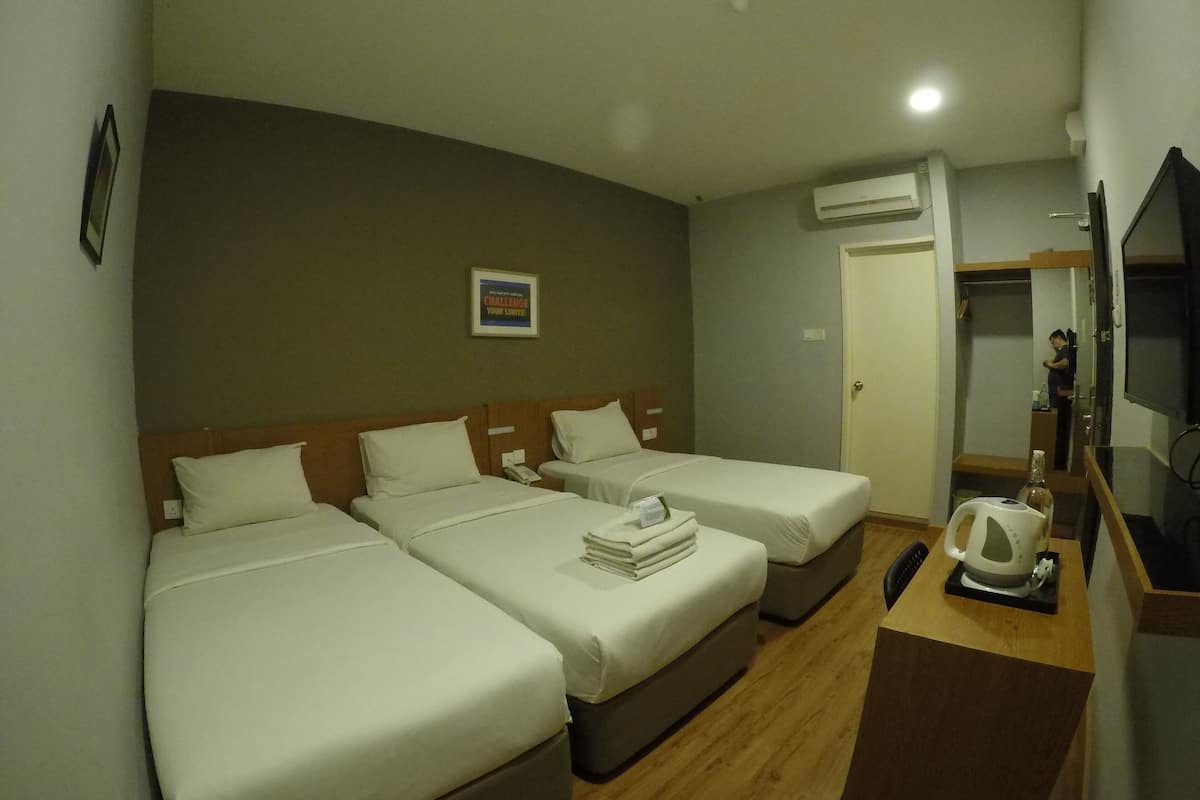 Quarto de hotel com duas camas de solteiro, uma escrivaninha de madeira com chaleira e uma televisão.