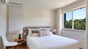 Una camera da letto con un letto, una sedia, un comodino, una finestra vista e un condizionatore d'aria a parete.