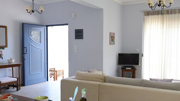 Ein Wohnzimmer mit einer Couch, einem Esstisch gedeckten Geschirr, einem Fernseher und einer Tür zu einem anderen Raum.