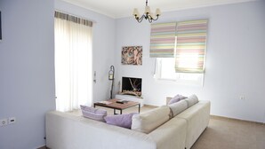 Ein Wohnzimmer mit einer Couch, einem Couchtisch und einem Fernseher. Es gibt ein Fenster mit Vorhängen und ein Bild an der Wand.