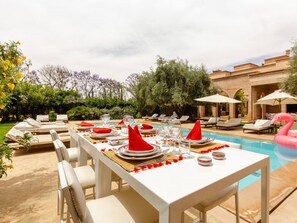 A poolside dining area with a table set for four, surrounded by lounge chairs and a pool.