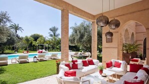 An outdoor lounge area with white furniture and red cushions, a pool, and lush greenery. - luxury 4 bedroom villa with heated swimming pool, 7 minutes from the center, quiet. (Marrakech)