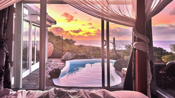 Una camera da letto con un'ampia finestra che si affaccia su una piscina e un panorama al tramonto.