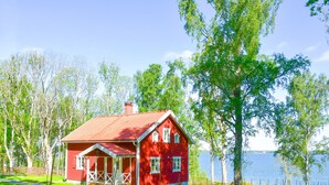 A red house with a porch, surrounded by trees and a body of water.