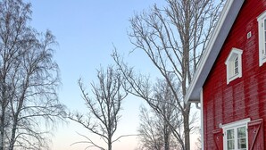 A red wooden house with a wooden deck and a view of a lake.