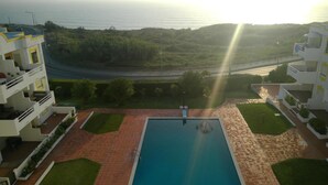 A swimming pool with a paved deck, surrounded by greenery and a view of the sea.