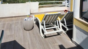 A balcony with a view of the sea, a yellow lounge chair, a small round table, and a bottle.