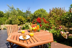Una mesa de madera al aire libre con un plato de comida, un vaso de jugo de naranja y una botella de jugo.