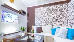 Una sala de estar moderna con una mesa de centro de vidrio, un sofá con cojines estampados, un televisor montado en la pared y un panel decorativo.