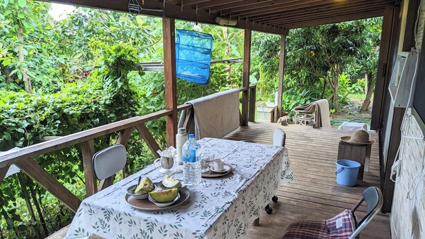 A covered outdoor dining area with a table set for two, surrounded by lush greenery. - TETRIS Guest House Kunisato (Isen)
