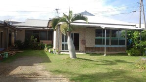 A two-story building with a flat roof, large windows, and a small garden area with a palm tree. - TETRIS Guest House Kunisato (Isen)
