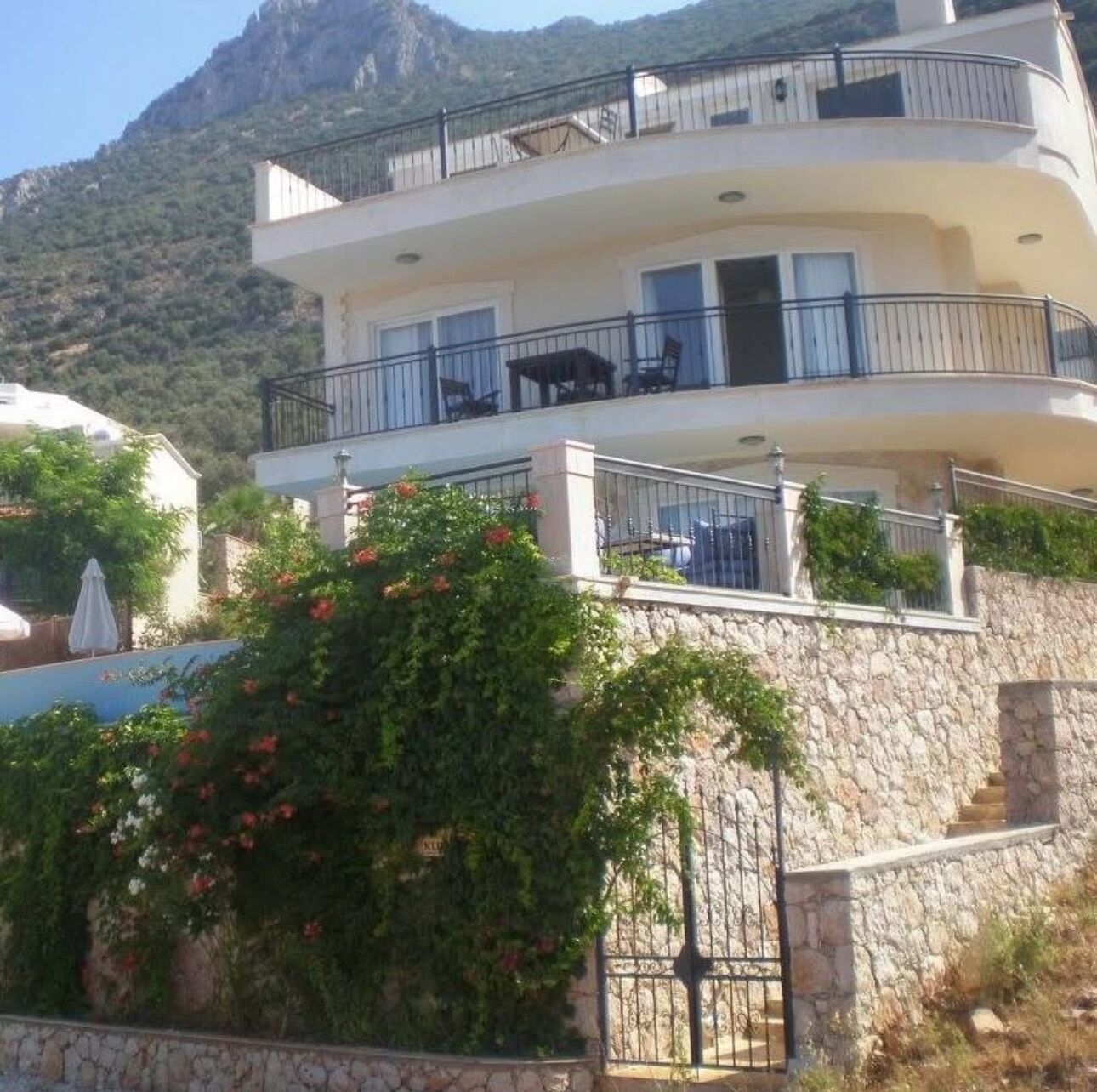 A multi-story building with balconies, stone walls, and a mountainous backdrop.
