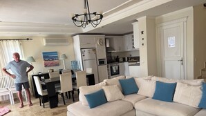 Ein Wohnzimmer mit einem beigefarbenen Ecksofa, einem schwarzen Couchtisch und einem Essbereich mit Tisch und Stühlen.