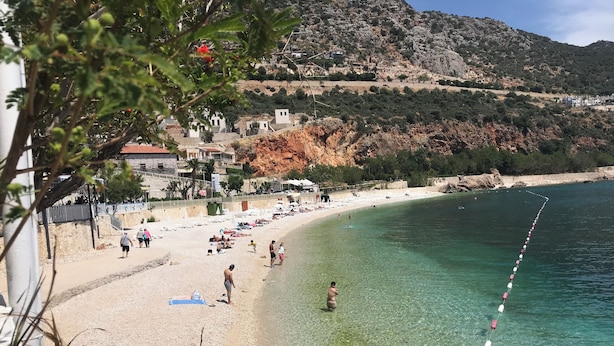 Ein Küstenstrand mit klarem Wasser, einem sandigen Ufer und einem Hintergrund aus felsigen Hügeln.