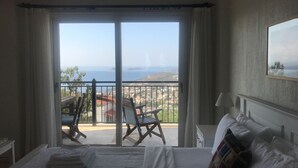 Ein Hotelzimmer mit Bett, Sessel und einem Balkon mit Blick auf das Meer und Gebäude.