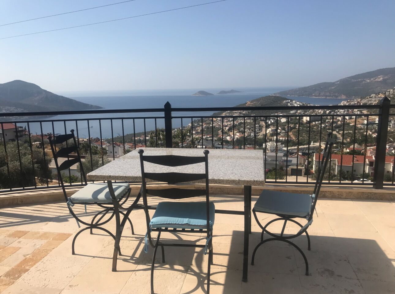Un balcón con una mesa y dos sillas, con vistas a un pueblo costero y montañas al fondo.