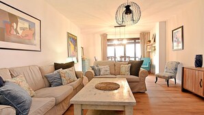 A living room with a beige sofa, a coffee table, and a patterned armchair. There is a dining area in the background with a table and chairs. - Spacious quiet apartment 450 meters to the beach, huge patio, communal pool. (Torre del Mar)
