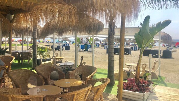 An outdoor seating area with wicker furniture and thatched umbrellas, overlooking a beach with umbrellas and lounge chairs. - Spacious quiet apartment 450 meters to the beach, huge patio, communal pool. (Torre del Mar)