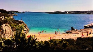 Una spiaggia costiera con acque blu cristalline, scogliere rocciose e alcune persone che ammirano il panorama.
