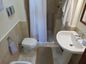 A small bathroom with a toilet, shower, and sink.