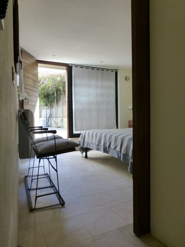 Une petite pièce bien éclairée, avec un lit, une chaise et une fenêtre avec des rideaux.