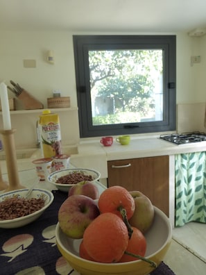 Une cuisine avec une fenêtre, un saladier rempli de fruits et divers aliments disposés sur le plan de travail.