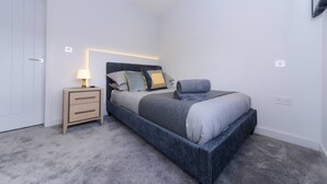 Ein Schlafzimmer mit Bett, Nachttisch, Lampe und Wandleuchte.