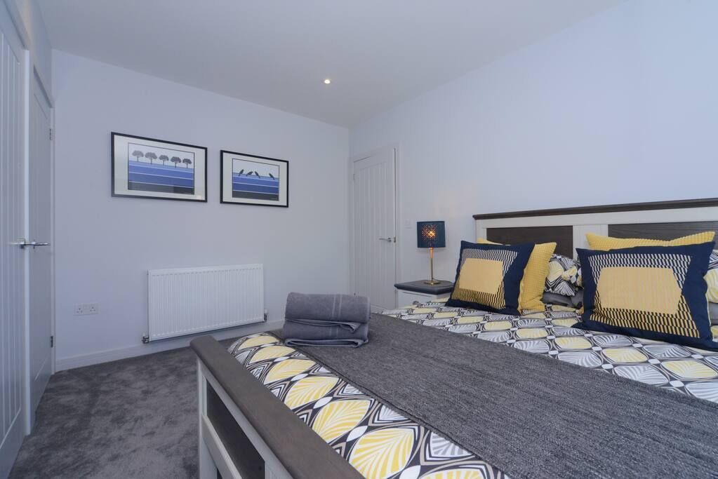 A bedroom with a large bed, a bedside table with a lamp, and two framed pictures on the wall.