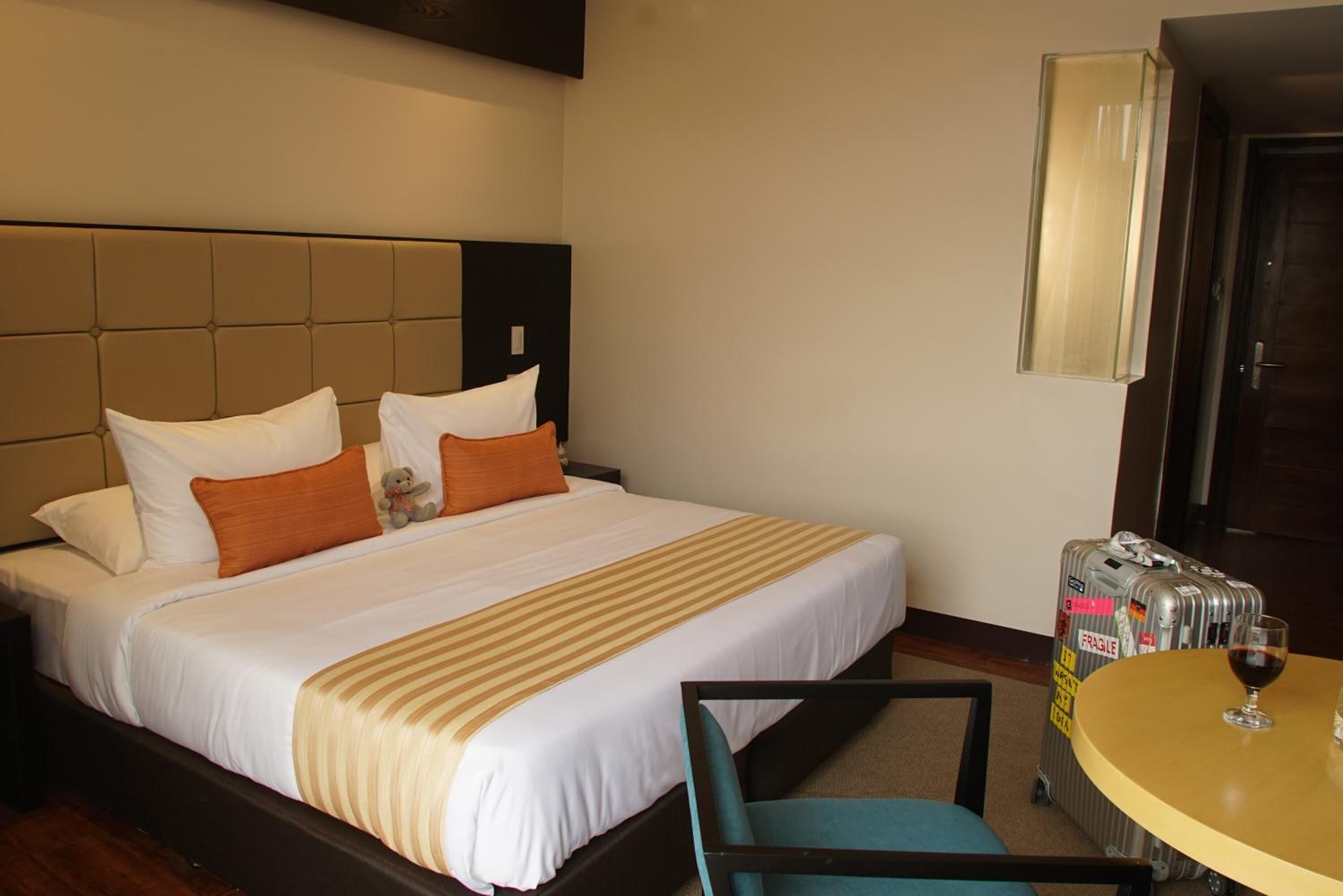Une chambre d’hôtel avec un grand lit, une table de chevet sur laquelle se trouve un verre de vin, et une valise.