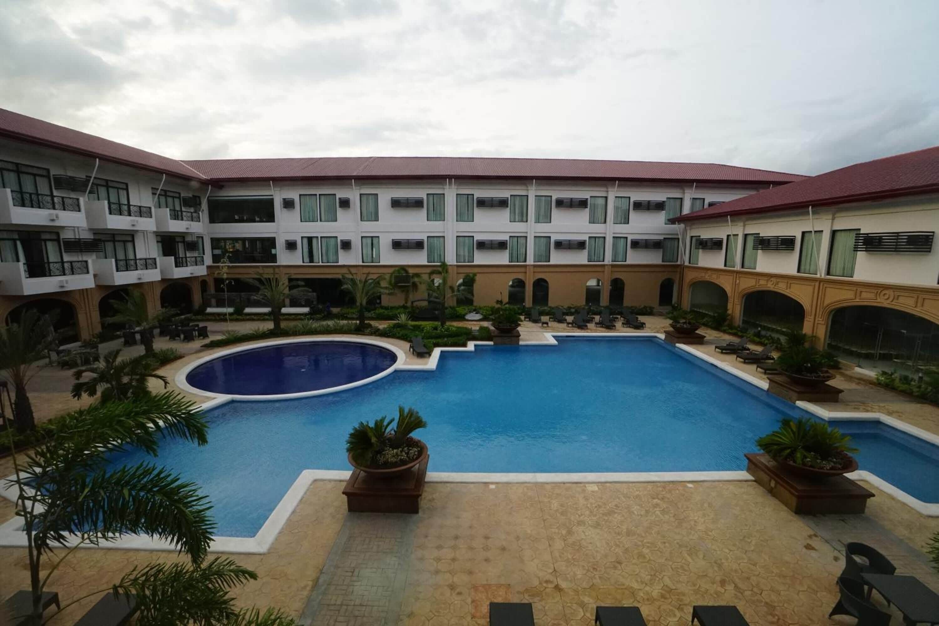 A hotel courtyard with a central swimming pool, multiple balconies, and outdoor seating areas.