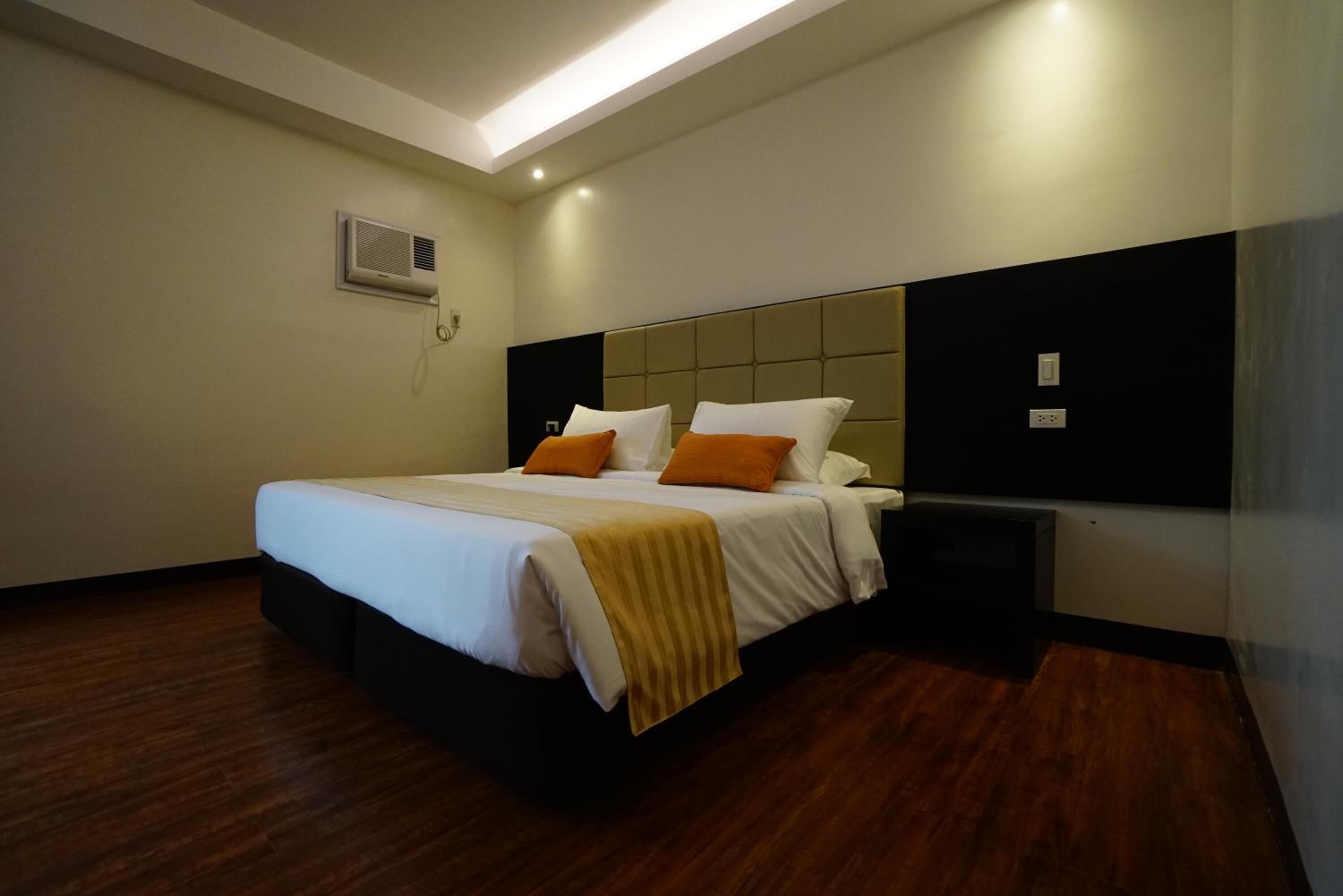 A modern hotel room with a large bed, a headboard, a bedside table, and an air conditioning unit on the wall.