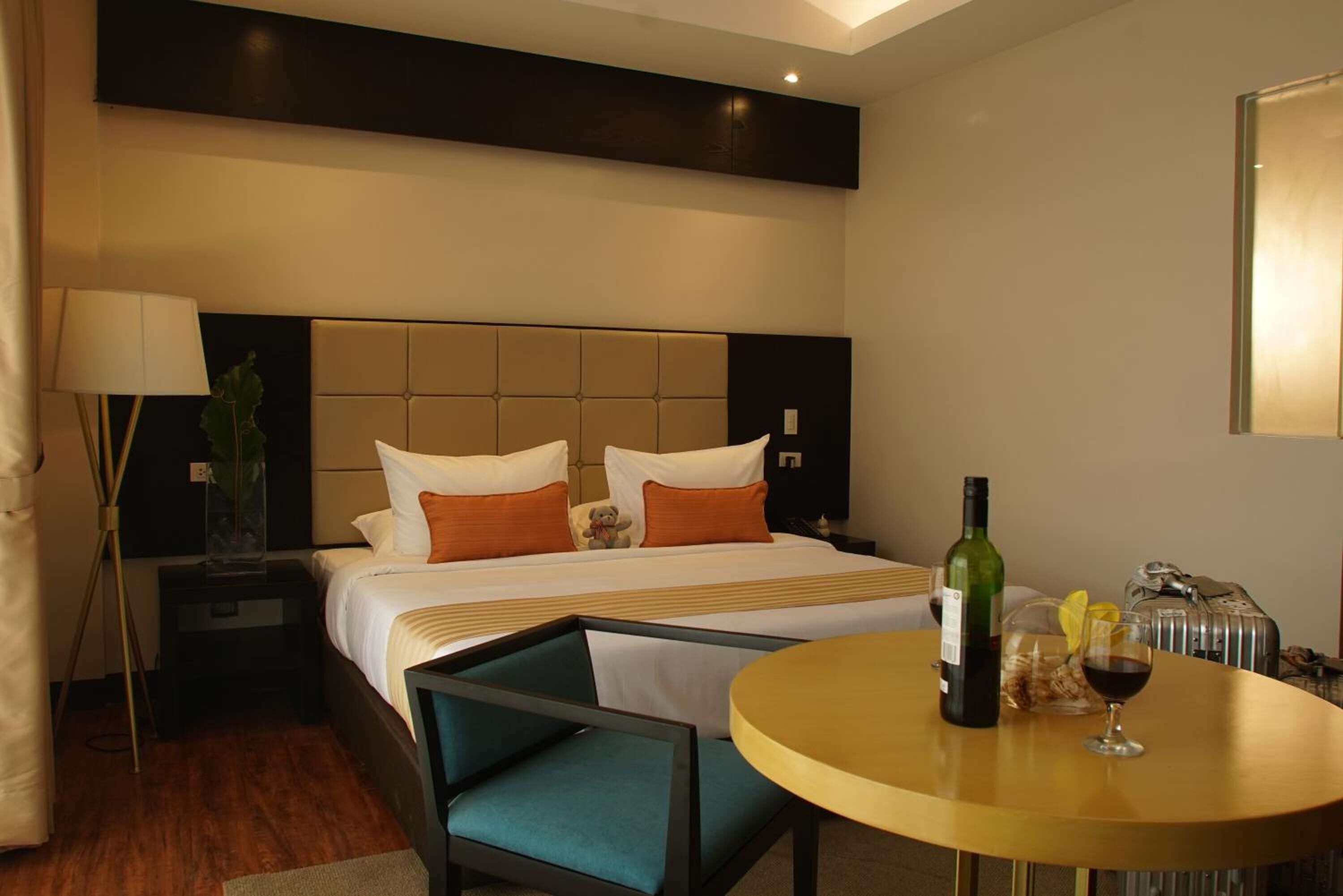 A hotel room with a bed, bedside table, lamp, and a round table with a bottle and glass.