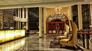 A lobby with a reception desk, a chandelier, a sofa, and a large arched window. - Hotel Oazis Butuan (Butuan)