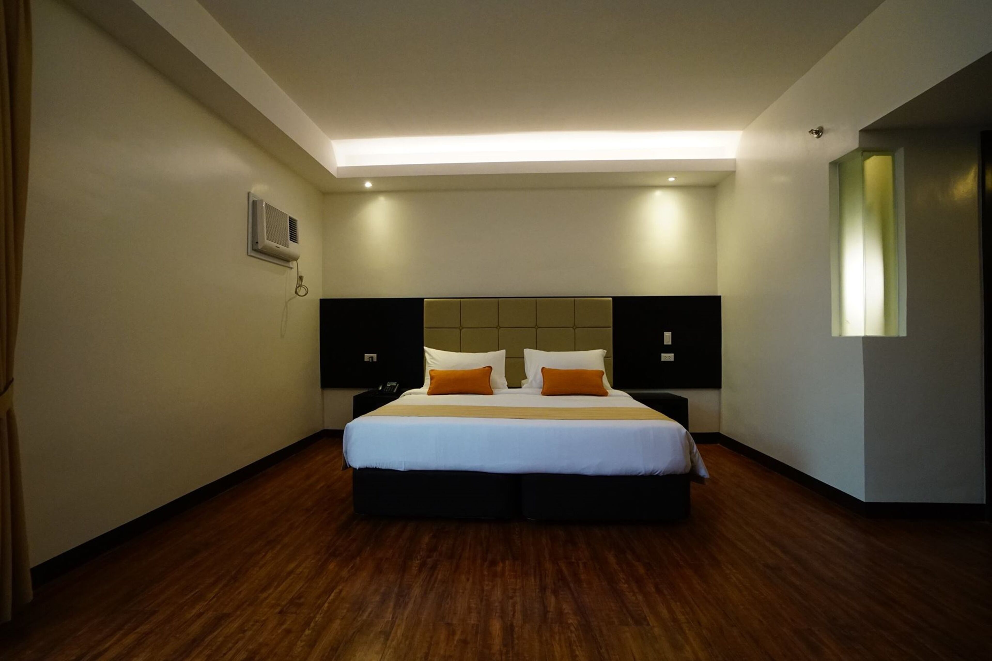 Una habitación de hotel moderna con una cama grande, dos mesitas de noche, una lámpara de techo y un aire acondicionado de pared.