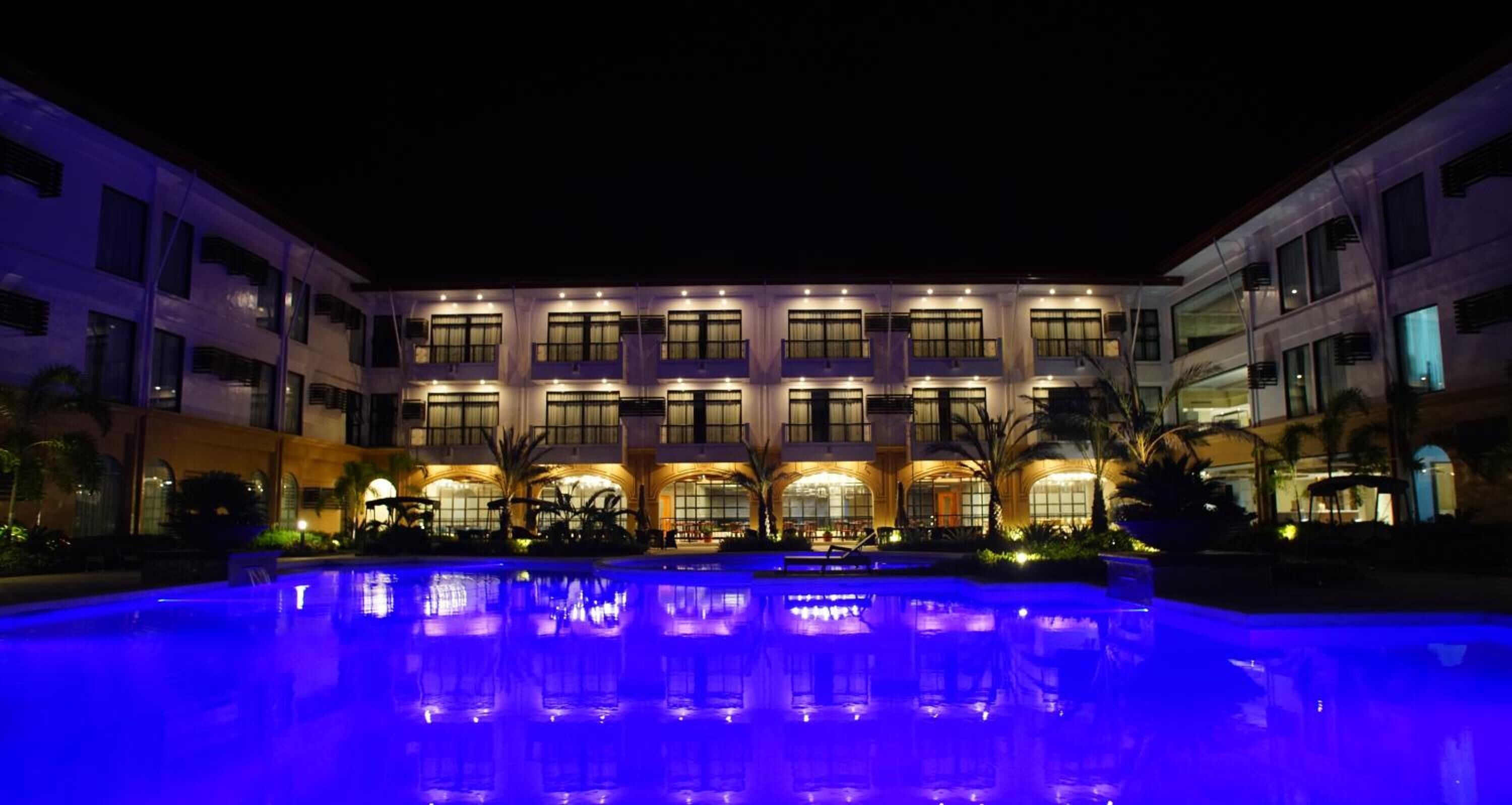 A hotel with a pool, multiple balconies, and a well-lit facade.