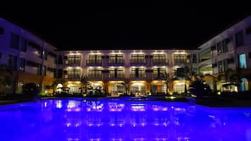 A hotel with a pool, multiple balconies, and a well-lit facade.