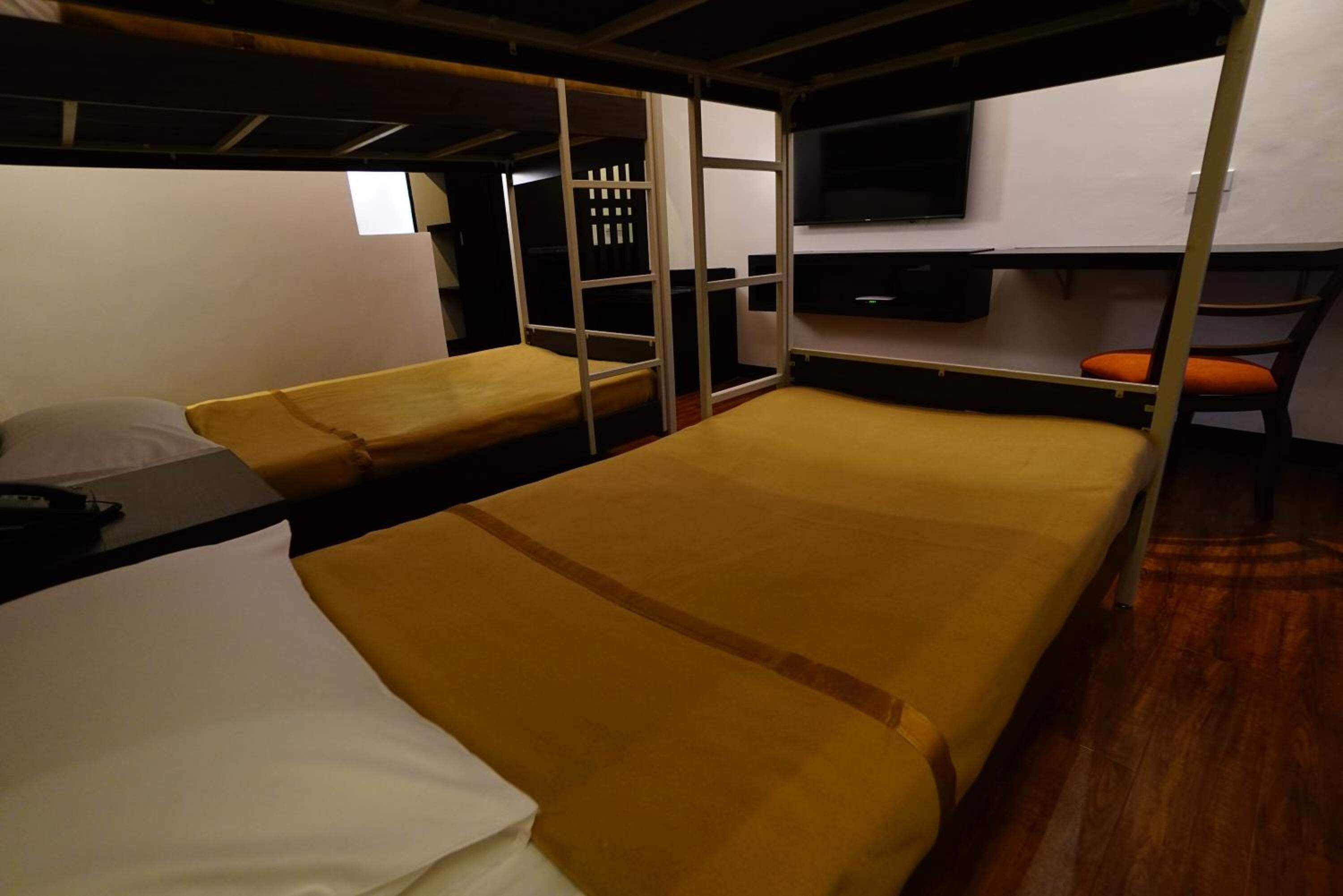 Ein kompaktes Zimmer mit Etagenbetten, einem kleinen Schreibtisch und einem an der Wand befestigten Fernseher.