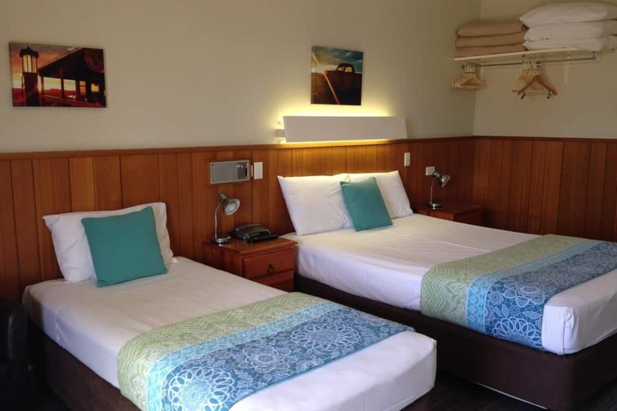 Quarto de hotel com duas camas, cabeceiras de madeira, mesas de cabeceira com luminárias e obras de arte nas paredes.