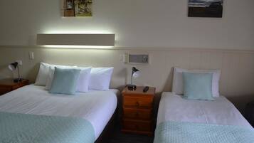 A hotel room with two beds, each with a white comforter and light blue pillows. There is a nightstand with a lamp and a remote control on one side.