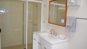 A bathroom with a glass-enclosed shower, a white sink with a mirror above it, and a towel hanging on a rack.